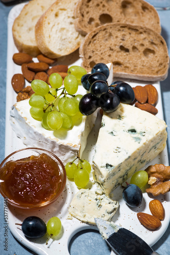 delicatessen cheeses on the board, fresh ciabatta, grapes and jams, vertical closeup