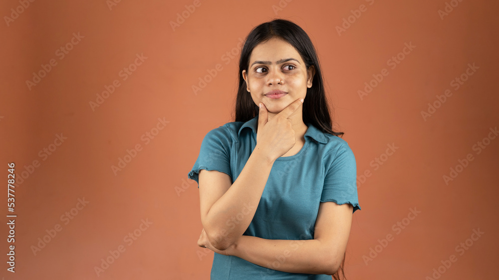 Obraz premium Pretty young woman looking up empty space deep thinking, holding arm on chin, isolated color background