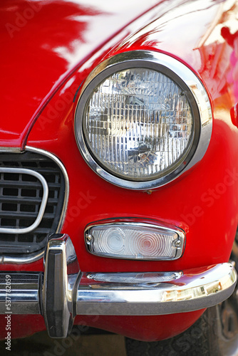 Round and chrome headlight on a red vintage car.