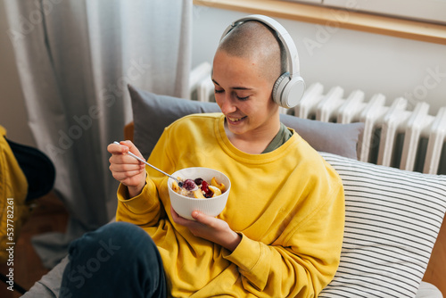 Tableau sur toile young bald woman with headphones eats fruit salad in her room