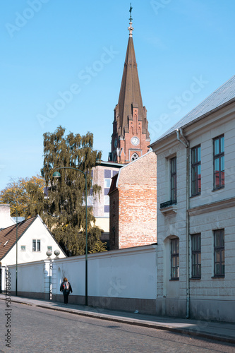 Woman walking along cobblestoned street in Lund Sweden with church Allhelgonakyrkan in the background photo