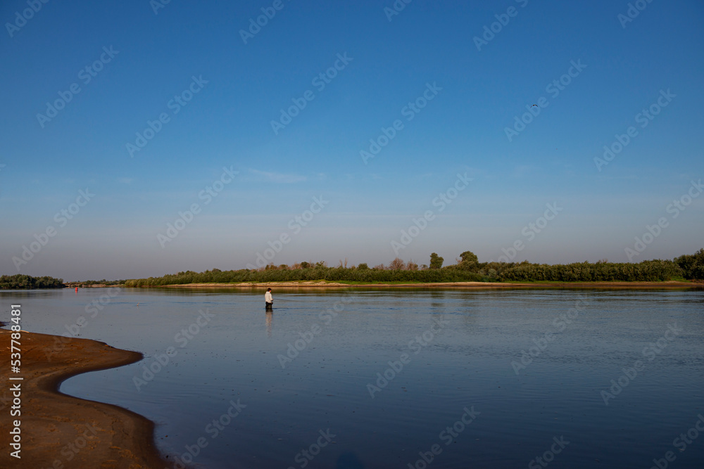 A fly-fishing fisherman on the river in summer.fly fishing fisherman in a gray jacket fishing in the middle of the river in the river in summer.copy space.bright advertising of fishing gear production