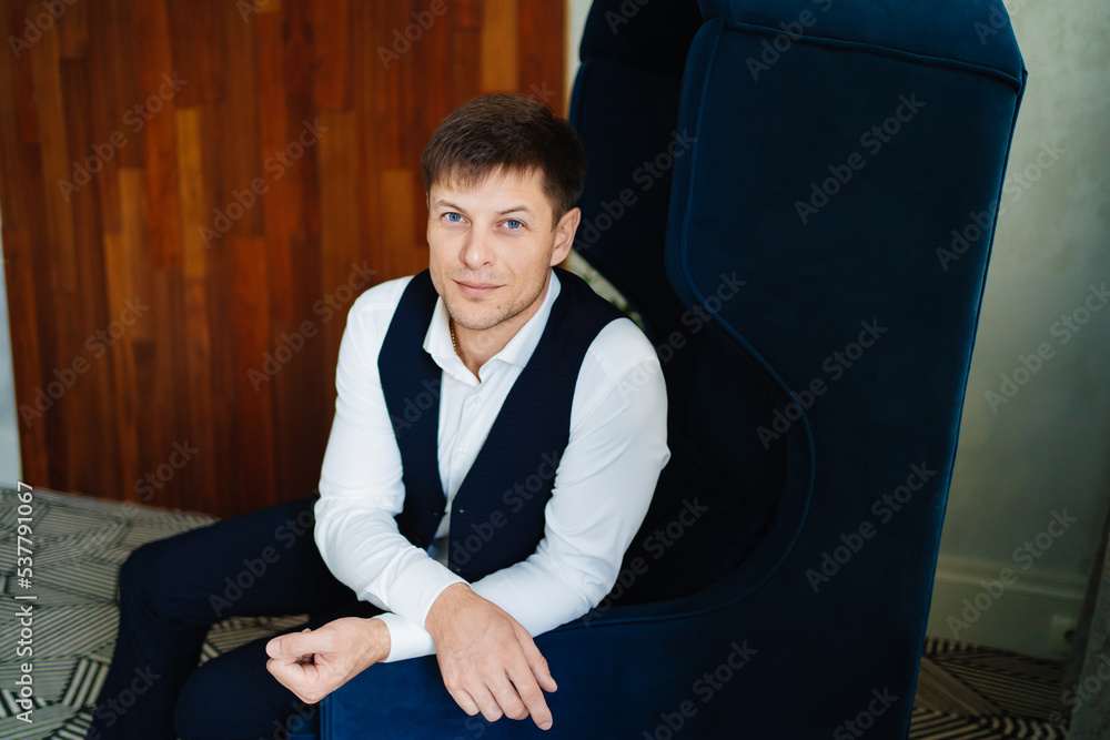 a man with a white shirt and a suit vest sits in a chair. a man with a white shirt and a suit vest sits in a chair.