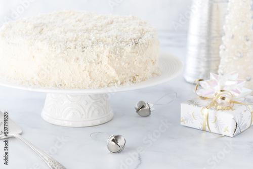 A coconut covered carrot cake surrounded by decorations all in white.