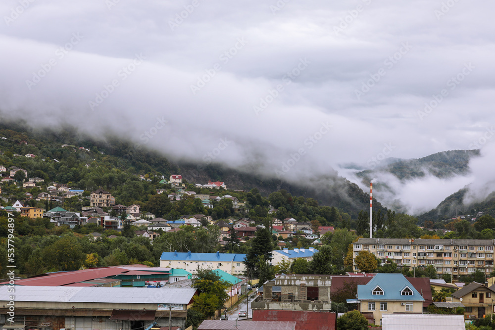 Fog over the city in the mountains. Picturesque autumn landscape. Smoking pipe boiler room pipe on the background of clouds. Sochi, Russia.