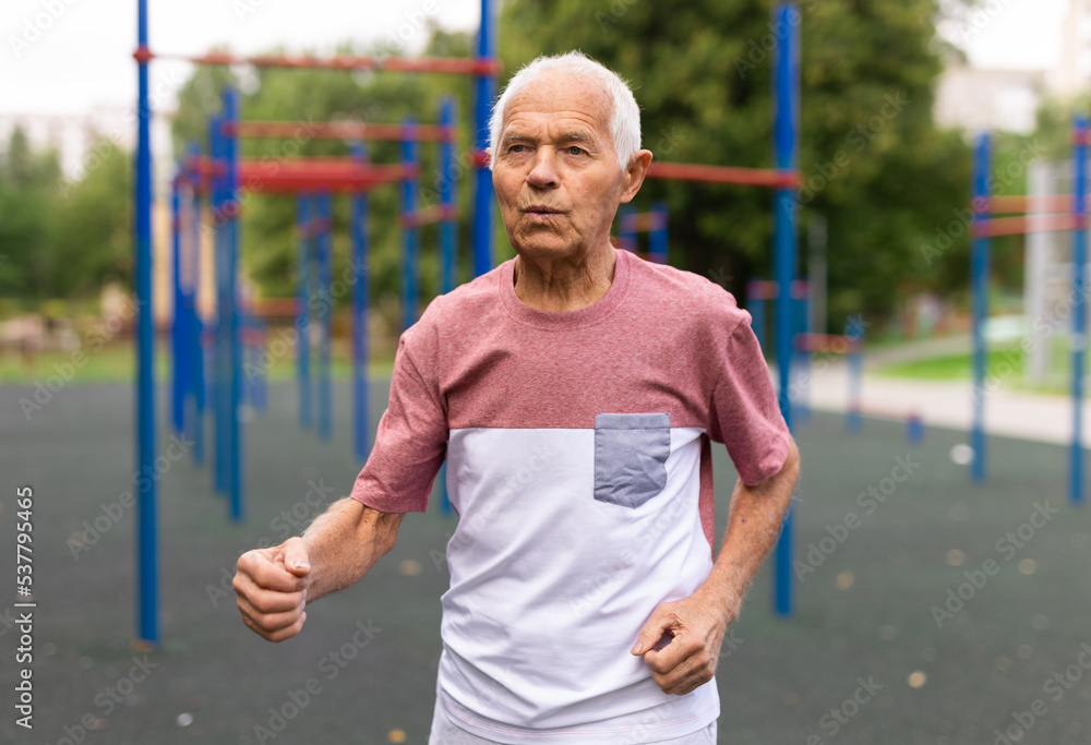Active senior man is jogging in summer park. Healthy retirement lifestyle