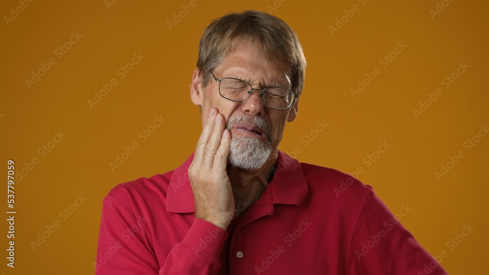 Mature handsome man in red shirt with tooth pain on yellow studio background. Male suffering from tooth ache, touching cheek, pulp inflammation, gingivitis Mature handsome man in red shirt with tooth pain on yellow studio background. Male suffering from tooth ache, touching cheek, pulp inflammation, gingivitis
