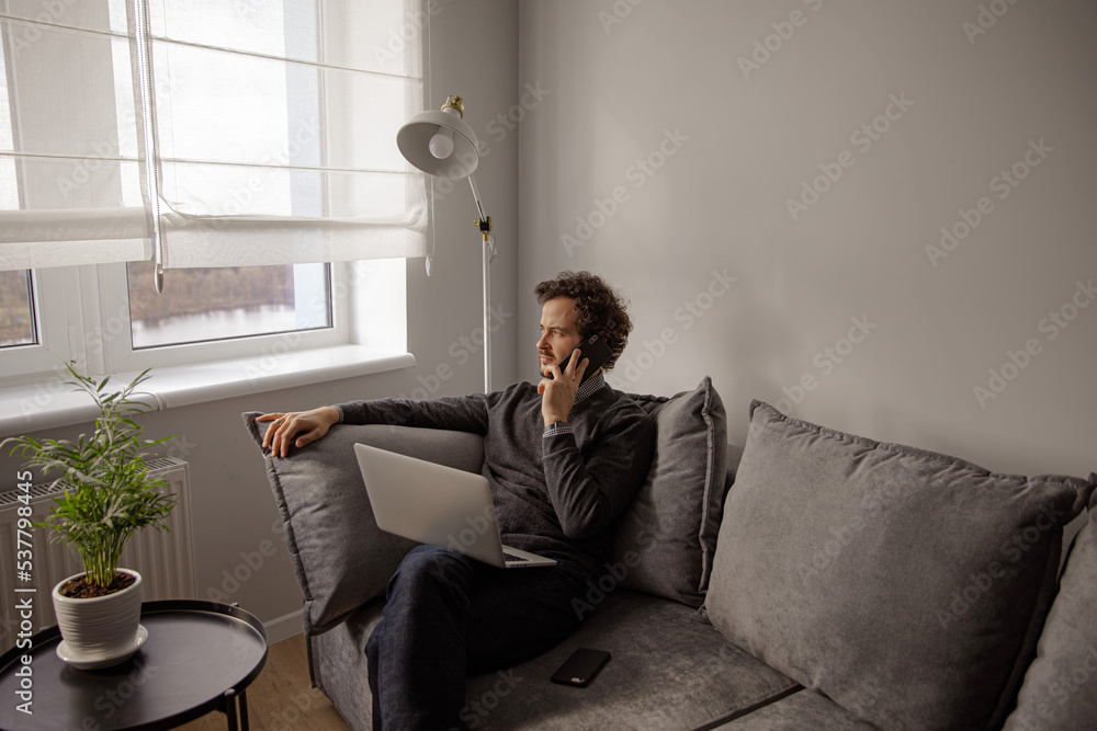 The guy solves serious questions over the phone. The man sits on a gray couch and talks on the phone. Work from home