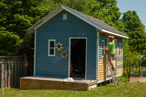 Man painting the exterior of a backyard shed