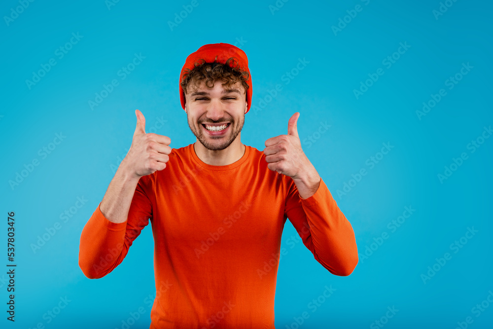 Young smiling man showing sight thumbs up and good luck on blue background Young smiling man showing sight thumbs up and good luck on blue background