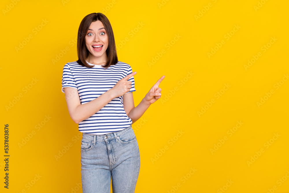 Photo of gorgeous lovely positive girl with wear striped t-shirt indicating empty space news promo isolated on yellow color background Photo of gorgeous lovely positive girl with wear striped t-shirt indicating empty space news promo isolated on yellow color background