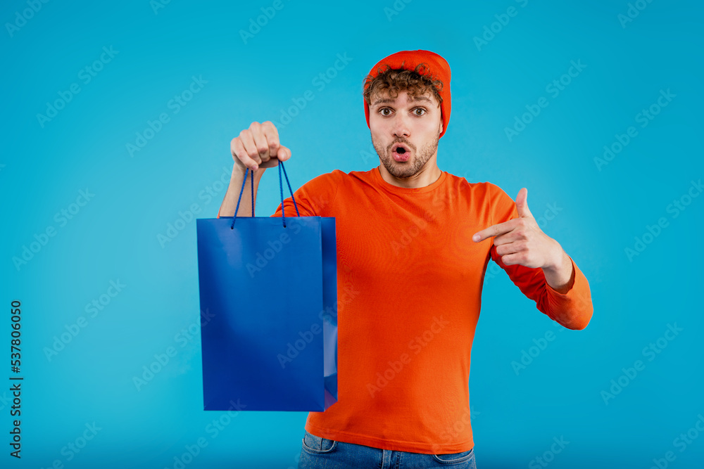 Young surprised man holds shopping bag on isolated blue background Young surprised man holds shopping bag on isolated blue background