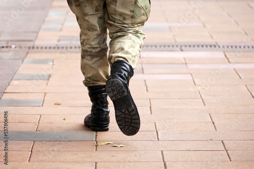 Soldier in military camouflage and boots walking down the city street, legs on sidewalk. Concept of service in army, mobilization photo