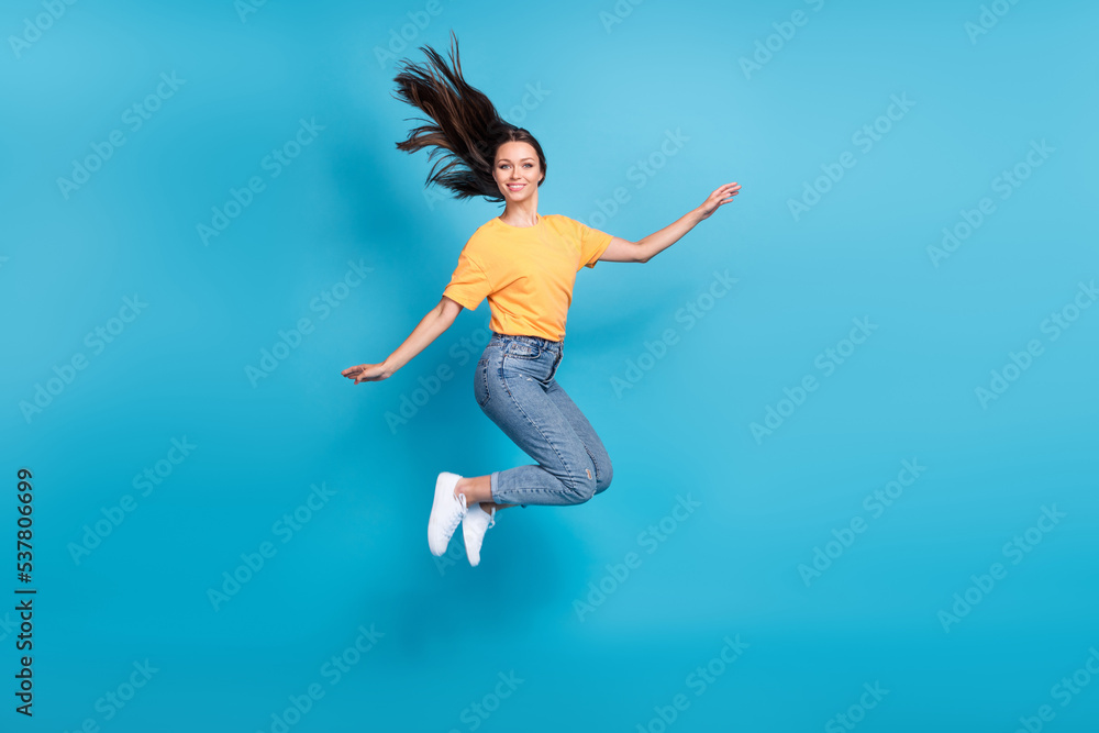 Full length photo of sweet shiny lady wear yellow t-shirt jumping high arms sides empty space isolated blue color background Full length photo of sweet shiny lady wear yellow t-shirt jumping high arms sides empty space isolated blue color background