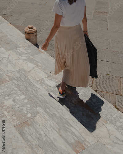 Happy young beautiful woman in summer outfit, white t-shirt and long skirt. Walking down the steps of church or old italian building. Happy day in Italy. 