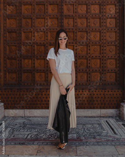 Fashionable curly woman. Happy young beautiful woman in summer outfit, sunglasses, white t-shirt and long skirt. Behind her wooden door of church or old italian building. Happy day in Italy. 