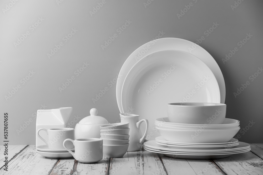 a set of white ceramic tableware on a light background. Various types of white plates, bowls and platters, cups, saucers, milkmen. Simple white tableware for use at home or in a cafe. a set of white ceramic tableware on a light background. Various types of white plates, bowls and platters, cups, saucers, milkmen. Simple white tableware for use at home or in a cafe.