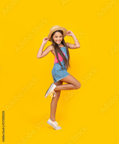 positive teen girl in straw hat running on yellow background