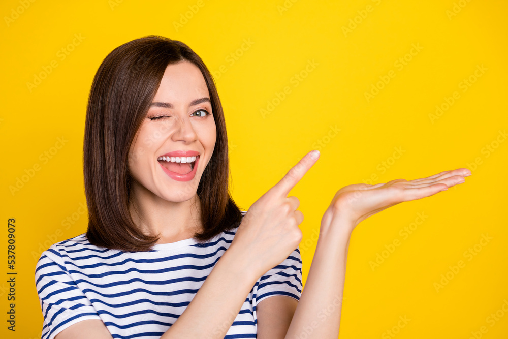 Photo of young attractive smiling cute woman blinking finger directing holding palm empty space advert isolated on yellow color background Photo of young attractive smiling cute woman blinking finger directing holding palm empty space advert isolated on yellow color background