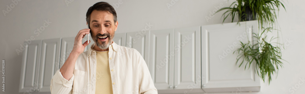 cheerful bearded man talking on mobile phone in kitchen, banner. cheerful bearded man talking on mobile phone in kitchen, banner.