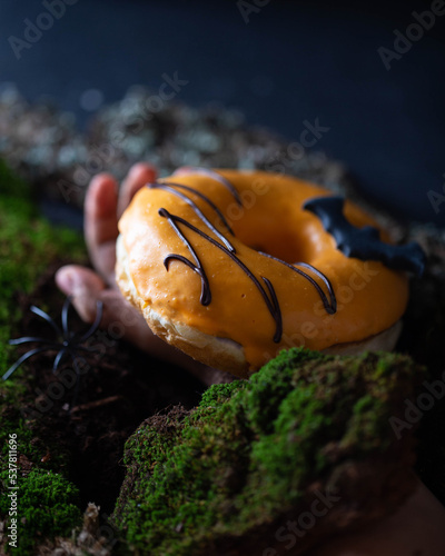 orange donut with spider and bat hand in ground moss halloween