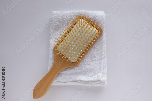 Wooden comb on white towel background. Modern paddle hair brush on table. Top view, flat lay, copy space. 
