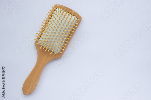 Wooden comb on white background. Modern paddle hair brush on table. Top view, flat lay, copy space. 