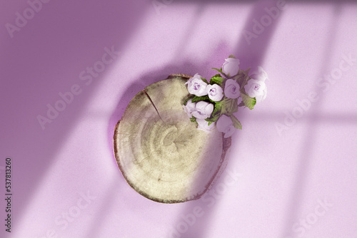 Product display podium with round wood and small flowers on the side. View from above. Blurred window shadow. photo