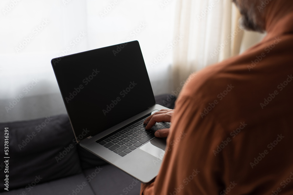 partial view of blurred man using laptop with blank screen at home. partial view of blurred man using laptop with blank screen at home.