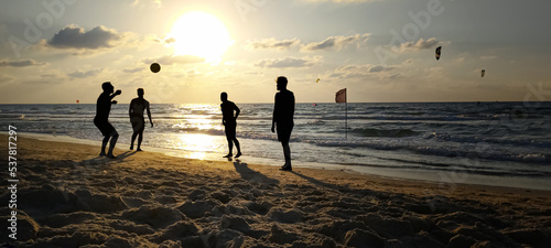 Beach, silhouettes of men playing a ball against the background of the sea and sunset. selective focus