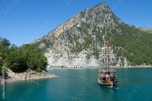 A three-masted tourist yacht floats on a lake among mountain cliffs near the Oymapinar dam. Green canyon, Manavgat, Antalya, Turkey