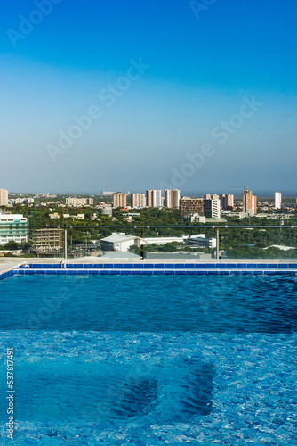 Barranquilla, Atlantico, Colombia. July 30, 2022: Swimming pool from a building and view towards the city with beautiful blue sky. © camaralucida1