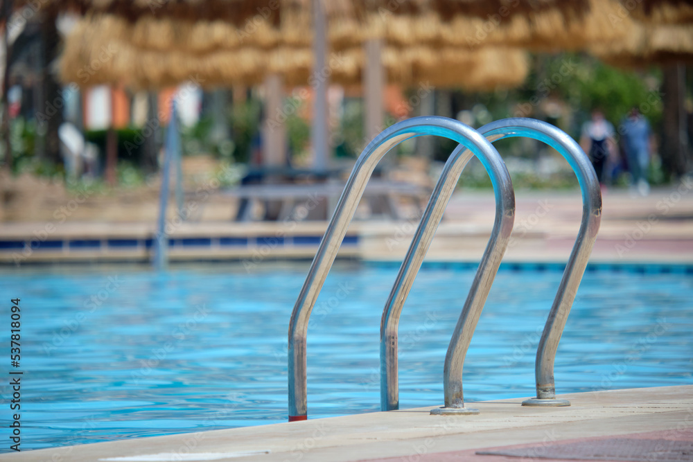 Close up of swimming pool stainless steel handrail descending into tortoise clear pool water. Accessibility of recreational activities concept Close up of swimming pool stainless steel handrail descending into tortoise clear pool water. Accessibility of recreational activities concept
