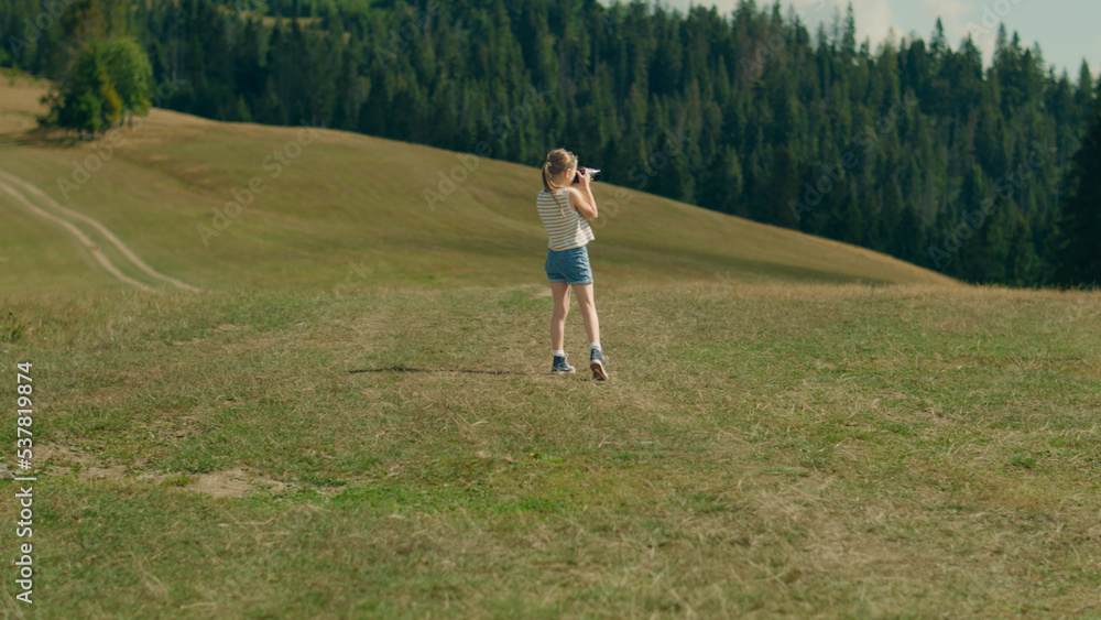 Young photographer walking on green hill and shooting beautiful nature landscape. Girl filling the portfolio with amazing photos, spending leisure time outdoor. Back view. Slow motion Young photographer walking on green hill and shooting beautiful nature landscape. Girl filling the portfolio with amazing photos, spending leisure time outdoor. Back view. Slow motion