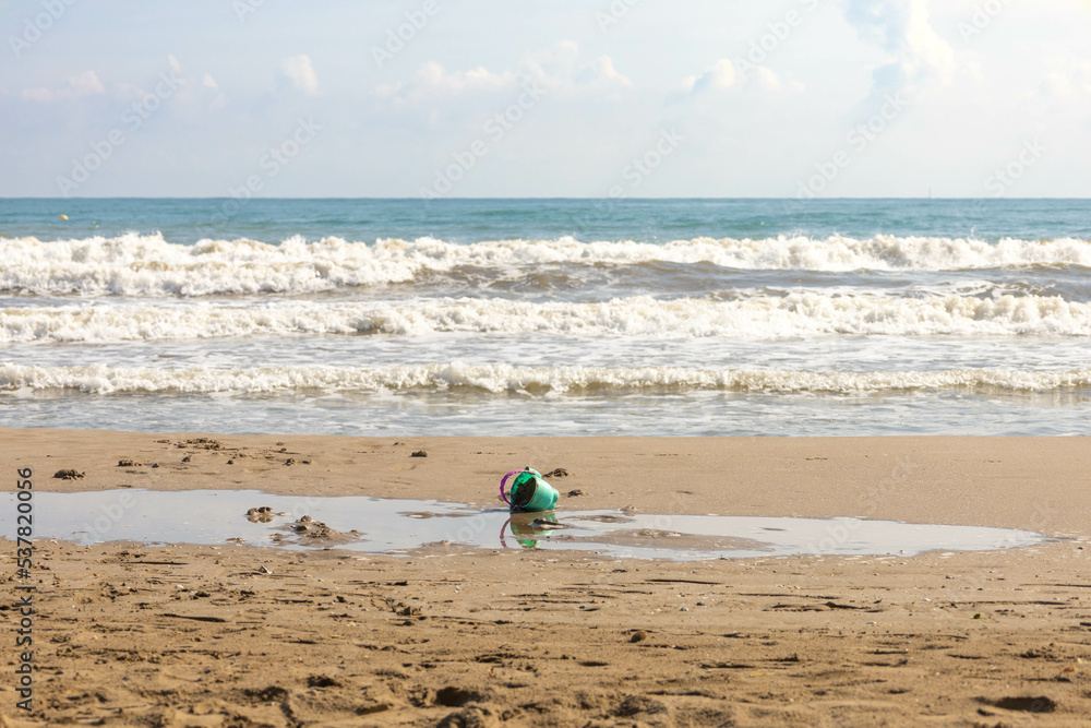 Beach in Valencia, Spain, Port Saplaya, where you can see a plastic bucket in the sand, and some waves in the Mediterranean sea Beach in Valencia, Spain, Port Saplaya, where you can see a plastic bucket in the sand, and some waves in the Mediterranean sea