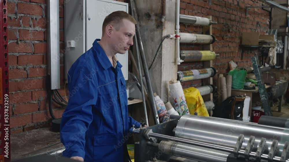 An engineer controlling the factory equipment stretching out the ecological textile material. An engineer monitoring the factory production equipment. Engineer observes factory manufacturing equipment An engineer controlling the factory equipment stretching out the ecological textile material. An engineer monitoring the factory production equipment. Engineer observes factory manufacturing equipment