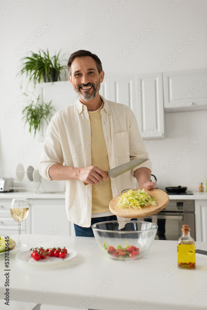 bearded man preparing salad with lettuce and cherry tomatoes while smiling at camera. bearded man preparing salad with lettuce and cherry tomatoes while smiling at camera.