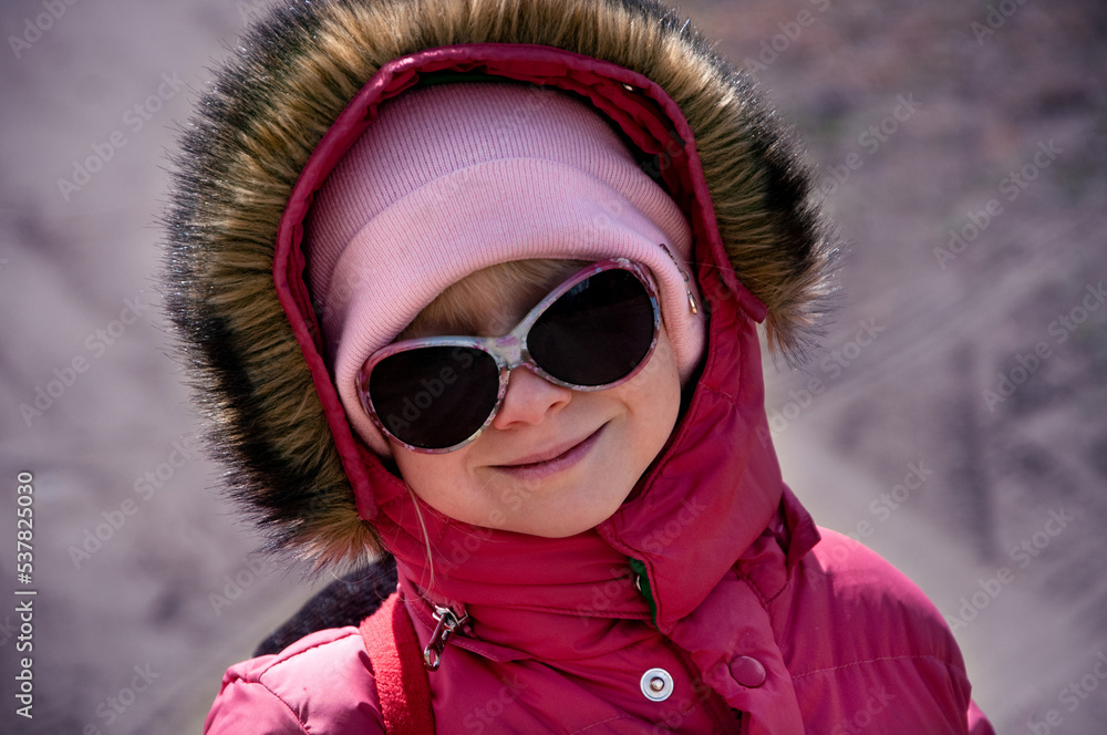 The girl smiles. Girl in a hood and sunglasses on a bright winter day. The girl smiles. Girl in a hood and sunglasses on a bright winter day.