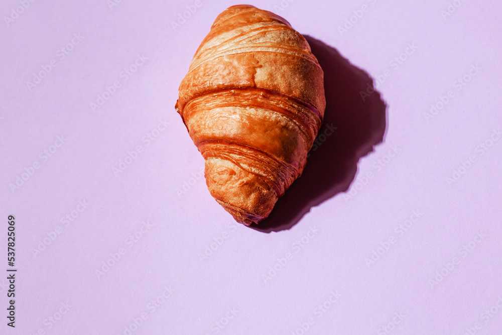 Lush and delicious croissant on a purple background. Creative concept of pastries and hearty breakfasts with space for text
