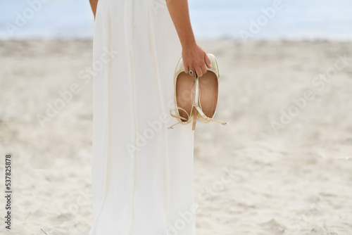 Fototapeta Naklejka Na Ścianę i Meble -  Bride in white dress and golden shoes on the beach