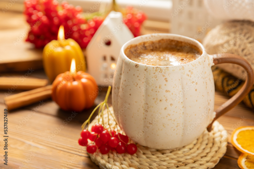 Autumn composition, a cup of hot coffee, a decorative little house, pumpkin candles, books and a warm sweater on a wooden table. Seasonal morning hot coffee. Cozy interior decor Autumn composition, a cup of hot coffee, a decorative little house, pumpkin candles, books and a warm sweater on a wooden table. Seasonal morning hot coffee. Cozy interior decor