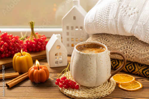 Autumn composition, a cup of hot coffee, a decorative little house, pumpkin candles, books and a warm sweater on a wooden table. Seasonal morning hot coffee. Cozy interior decor © Avocado_studio