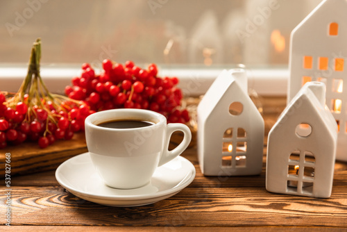 Autumn composition  a cup of hot coffee  a decorative little house  pumpkin candles  books and a warm sweater on a wooden table. Seasonal morning hot coffee. Cozy interior decor