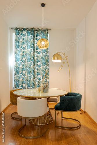 Front view dining room with modern table and chairs. There is a gold lamp and colored curtains photo