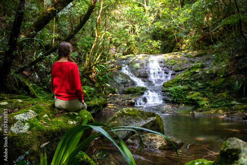 beautiful girl sits under a tropical waterfall in lamington national park  near gold coast in queensland  australia  waterfall in tropical rainforest in australia  rainforest walk