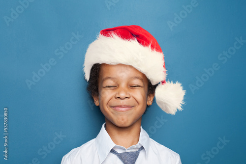 Happy black child boyin Santa hat makes a wish on blue background photo