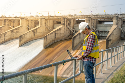 A dam engineering doing his checking routine. He is wearing a white hard hat and yellow transparent vest. He is standing by the rail by the dam. © Attayoot