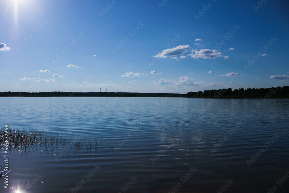 The water surface on the lake with a dense forest in the distance and clouds alying in the sky