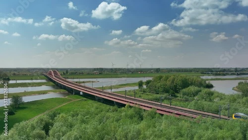 Train driving over the Hanzeboog train bridge over the river IJssel near the city of Zwolle in Overijssel during a springtime day. Aerial drone point of view. photo