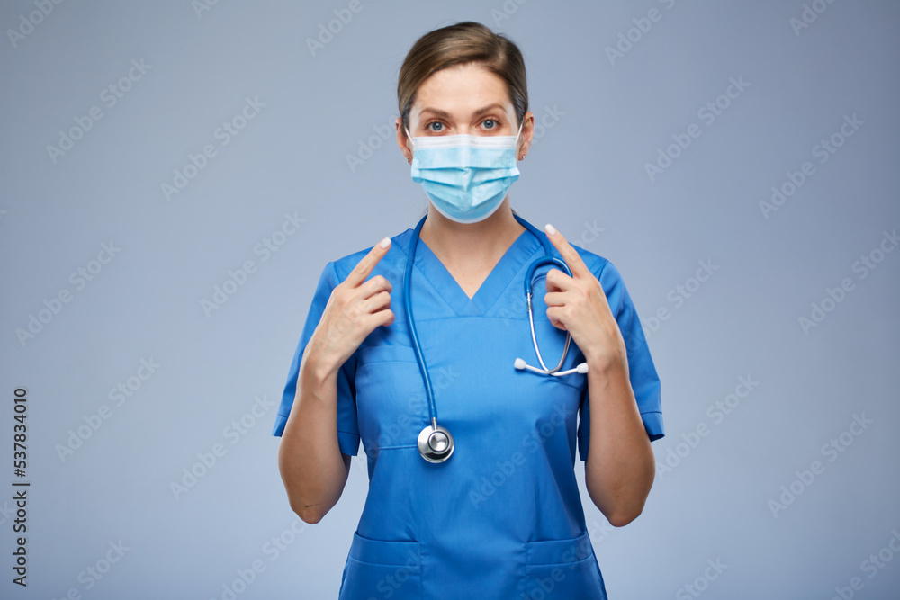 Nurse woman or doctor in blue medical mask points with two fingers. Isolated female portrait. Nurse woman or doctor in blue medical mask points with two fingers. Isolated female portrait.